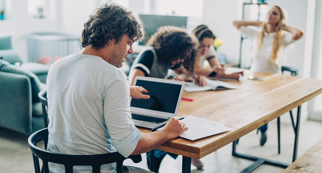 a photo of a family sitting a table teleworking and doing homework