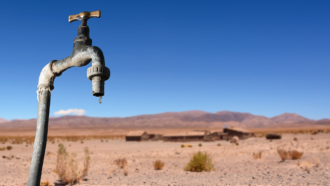 a photo of a water spigot with one drop of water hanging off of it, against a desert backdrop