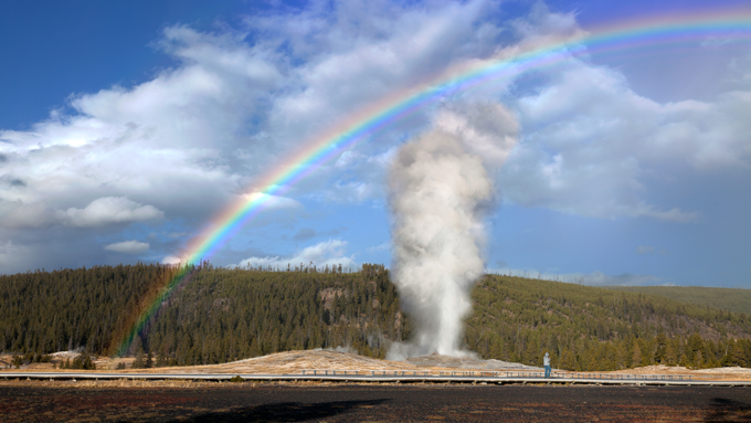 a photo of Old Faithful, a geyser in Yellowstone Park, shooting water up into the sky under a rainbow