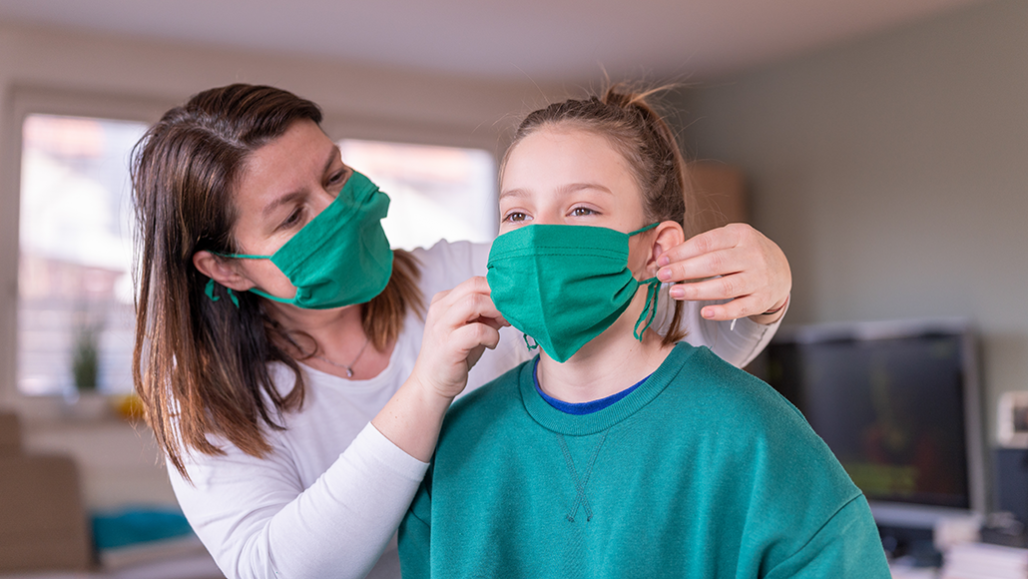 a woman fitting a homemade cloth mask on a teenage girl