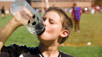 a photo of a sweaty boy drinking from a water bottle on a playing field