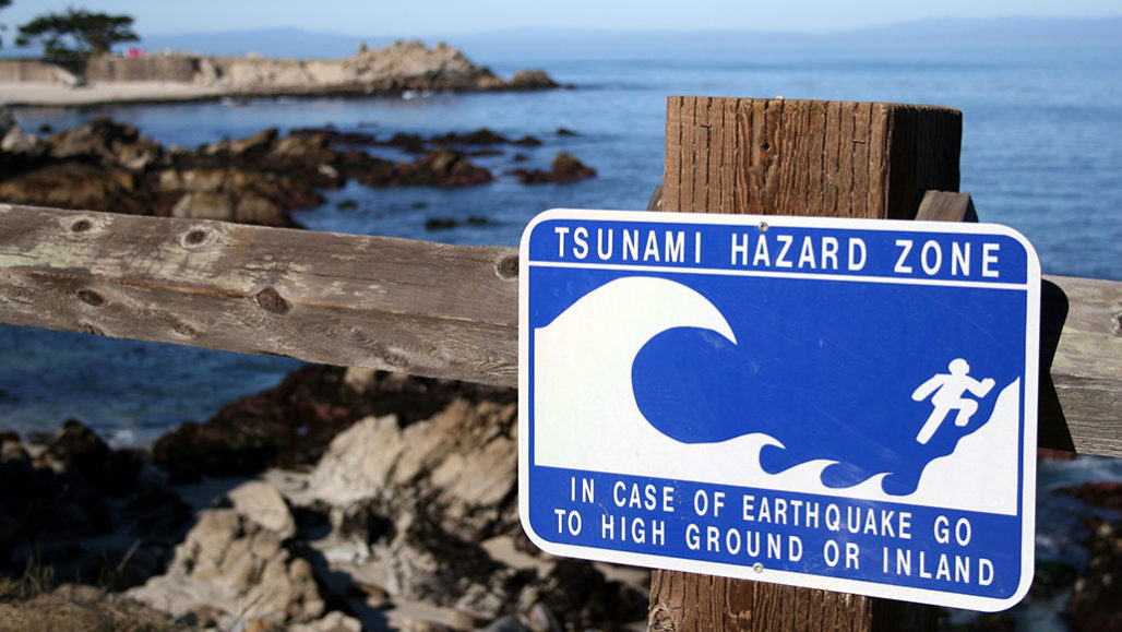 a photo of a tsunami hazard zone sign on a wooden fence near the shoreline