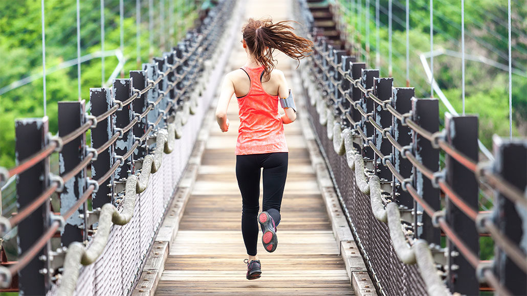 a photo of a woman with a ponytail running across a suspension bridge