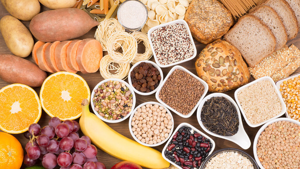 a top-down photo of grains, fruit, bread and beans on a table
