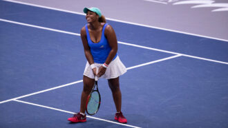 a photo of Taylor Townsend on the tennis court holding a raquet and smiling