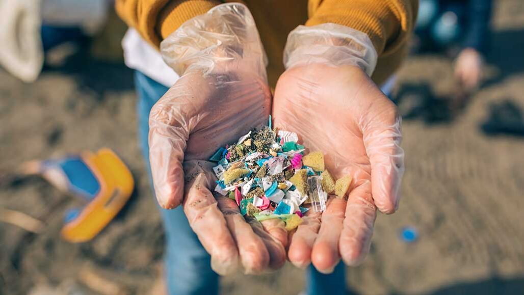 two plastic covered hands held together and palm up are holding lots of small pieces of plastic trash