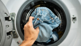 a photo of a hand putting a pair of blue jeans in a washer