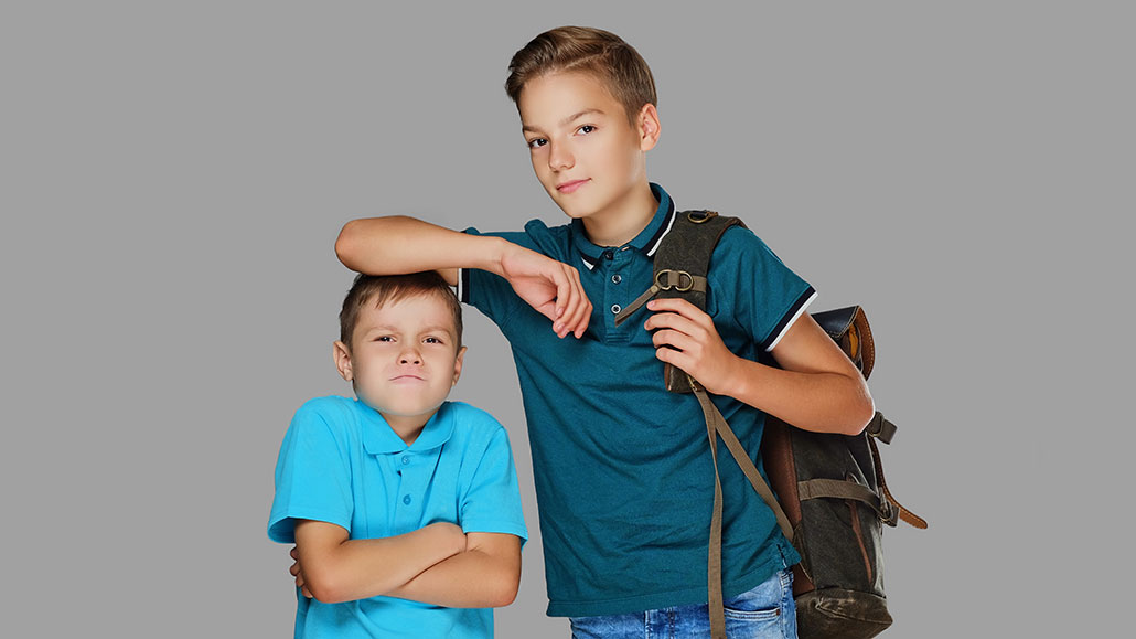 a tall boy resting his elbow on the top of a short boy's head - the short boy looks mad