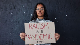 a black teen holding a sign that reads "RACISM is a PANDEMIC too"