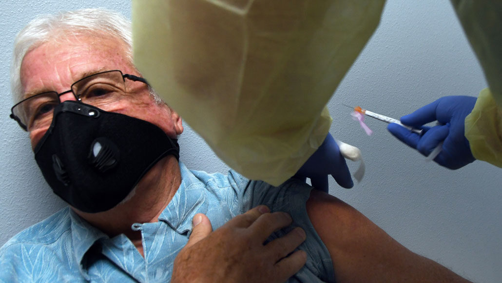 older man wearing a mask receiving a shot