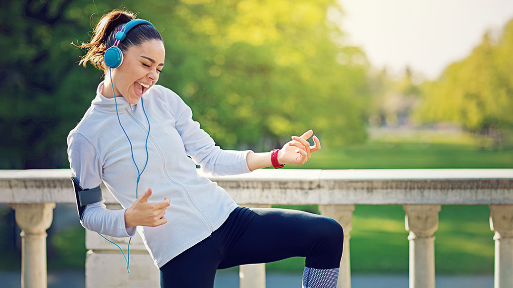 a girl wearing excercise clothing and headphones jams out on an air guitar