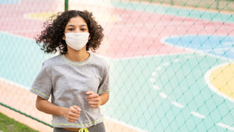 a girl wearing a face mask and jogging past a basketball court