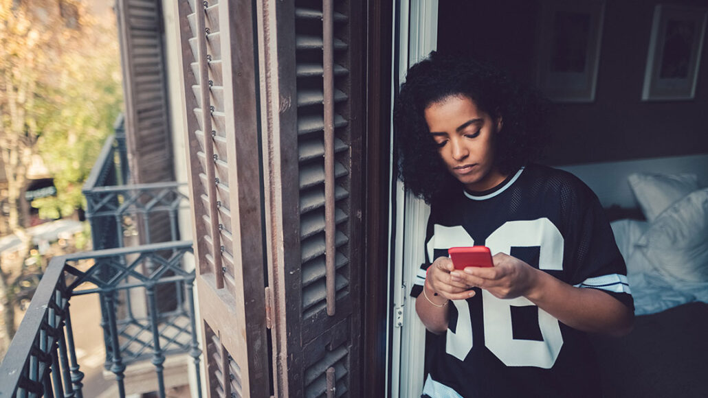 a woman leans against a window and looks sadly at her phone