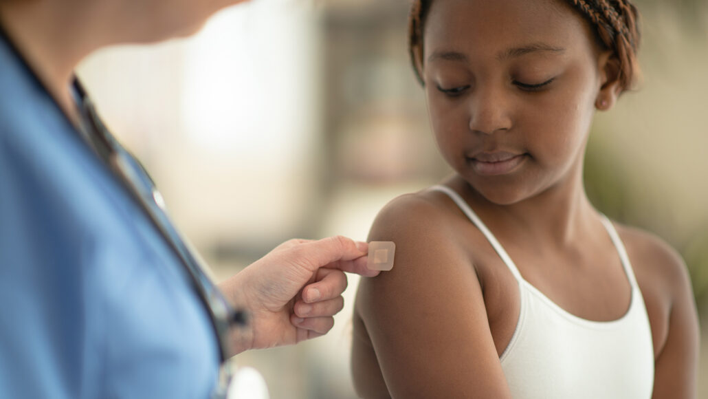 a little Black girl getting a peach-tented bandaid from a nurse