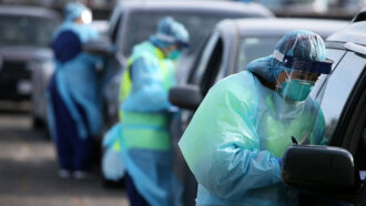 a photo of healthcare workers testing people in cars at a drive-up site