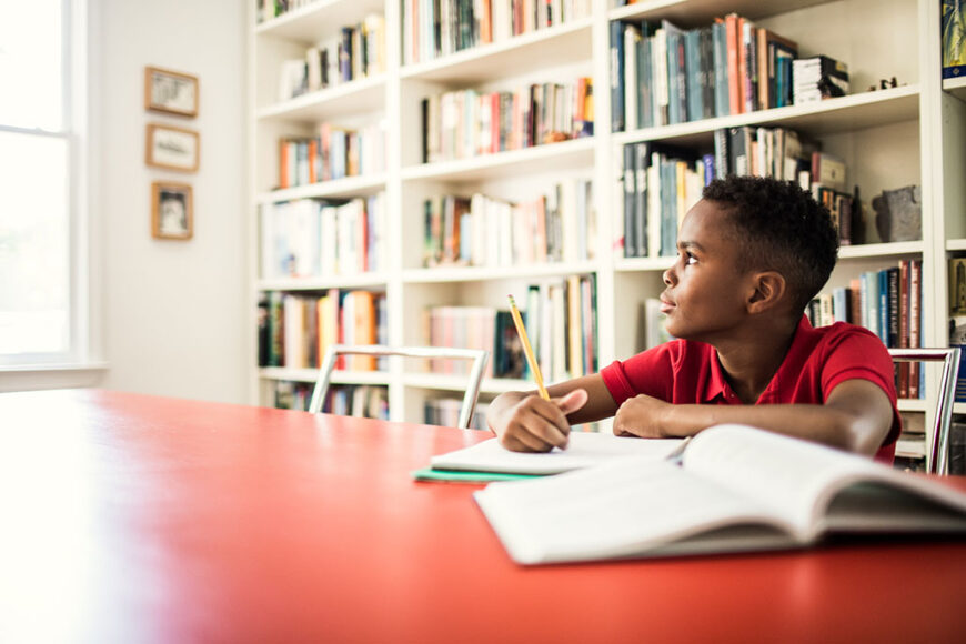 a photo of a boy sitting at a table in a library and daydreaming
