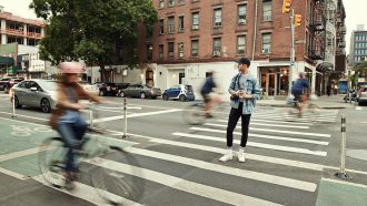 a person crossing the street in an urban setting cars and bikes are blurred in motion around them