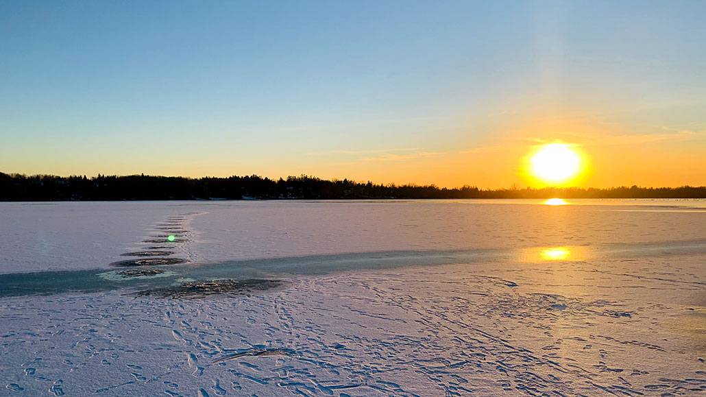 a photo of a frozen lake, the sun is just above the horizon
