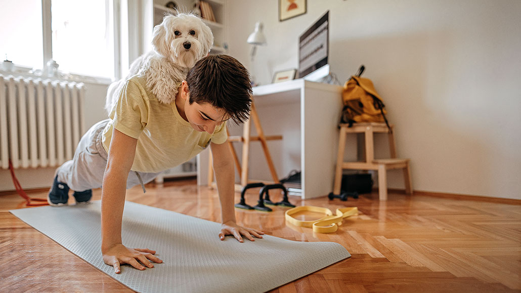 a boy on a yoga mat in pushup position with a cute white dog on his back