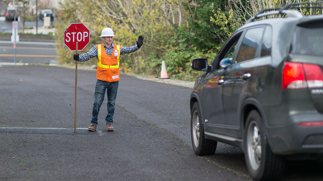 an SUV stopped in front of a stop sign held by a construction worker