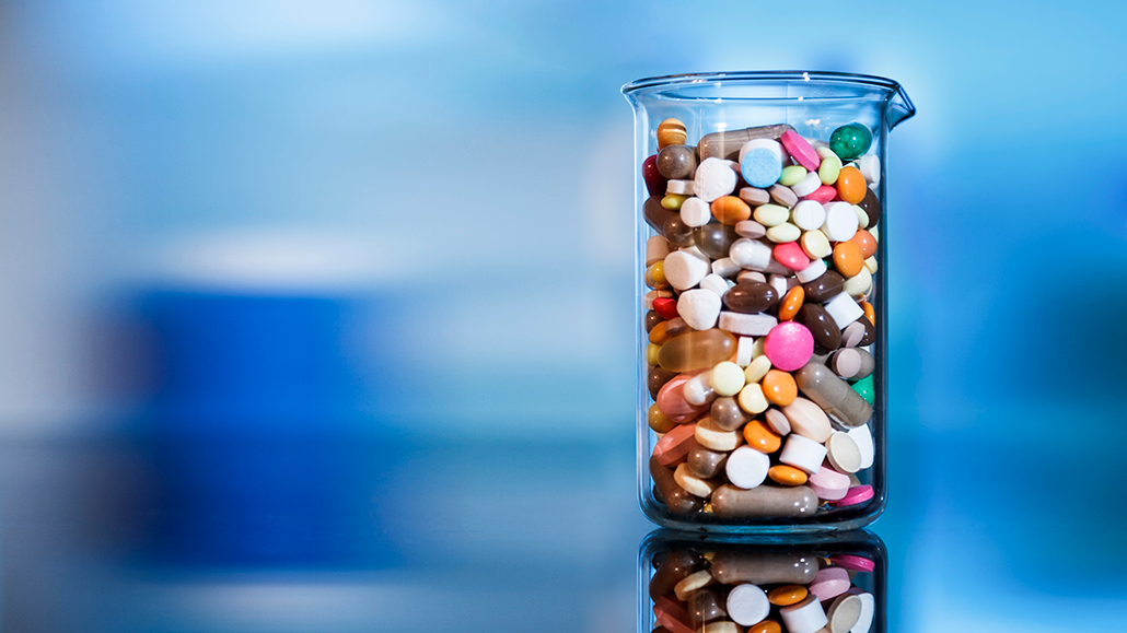 a small glass beaker full of pills of different shapes, sizes and colors