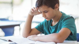 a photo of a boy reading with his hand on his head concentrating