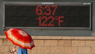 person walking by an electronic sign in Phoenix that reads 122 degrees and 6:27pm