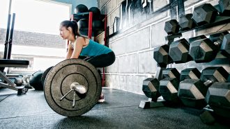 a picture of a gym with a lady squatting and holding a barbell with weight before lifting it