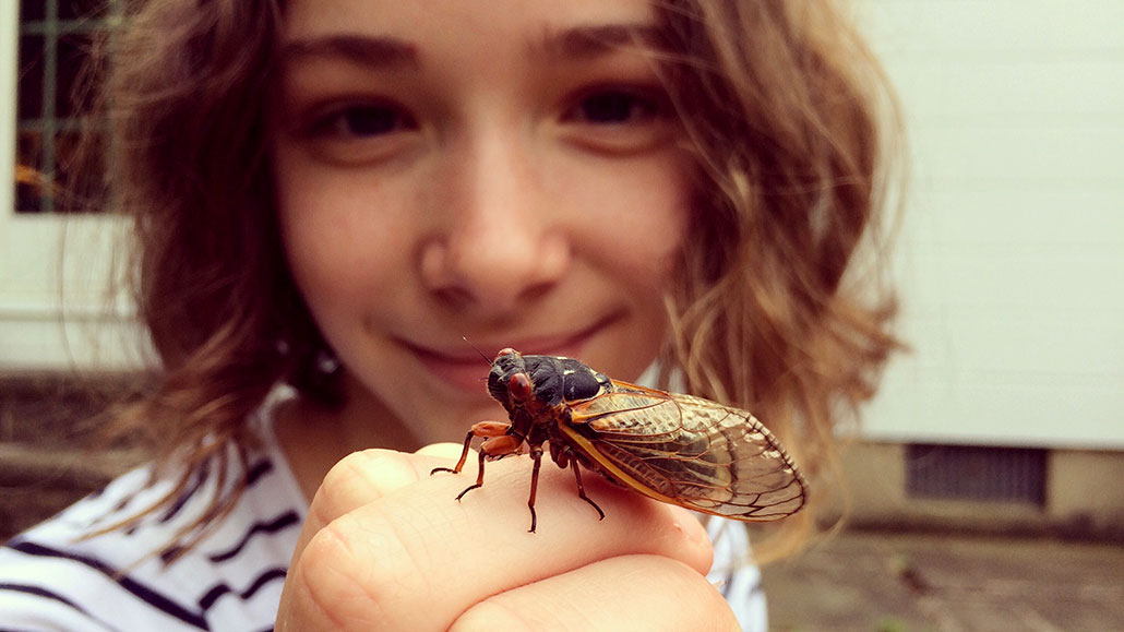 a girl smiling and holding a cicada up to the camera