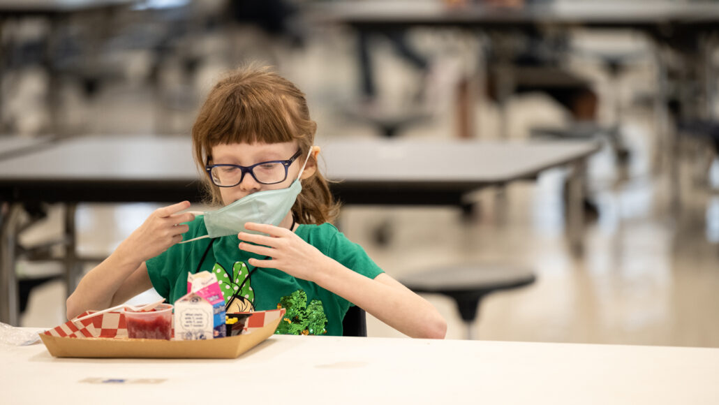 child removing a mask to eat lunch in a school cafeteria
