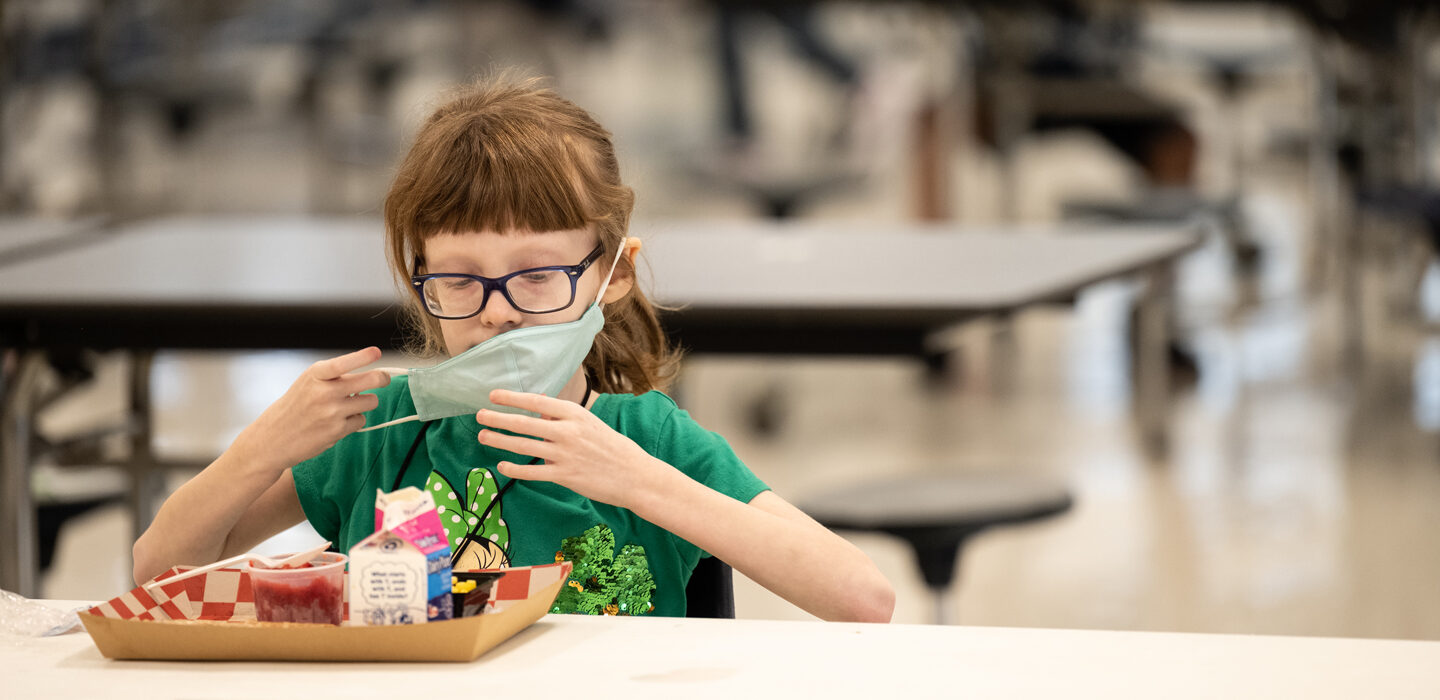 child removing a mask to eat lunch in a school cafeteria