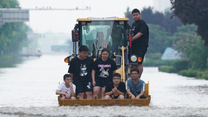 people riding in a backhoe amid flooding in China