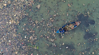 a canoe floats through water cluttered with plastic trash