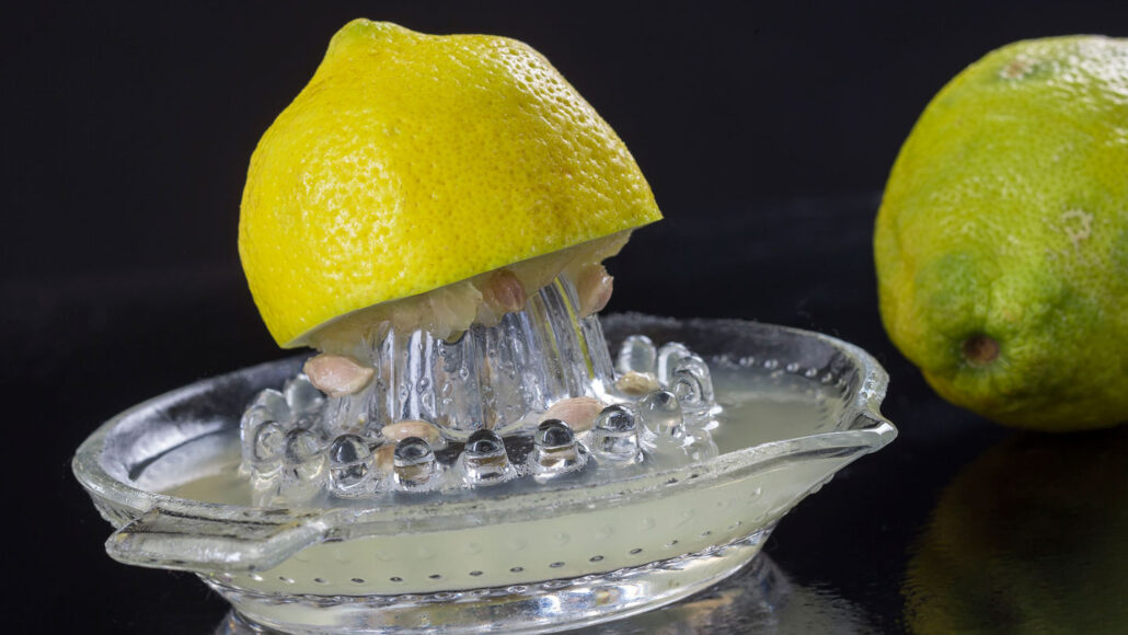 a lemon sits partially squeezed atop a lemon juicer