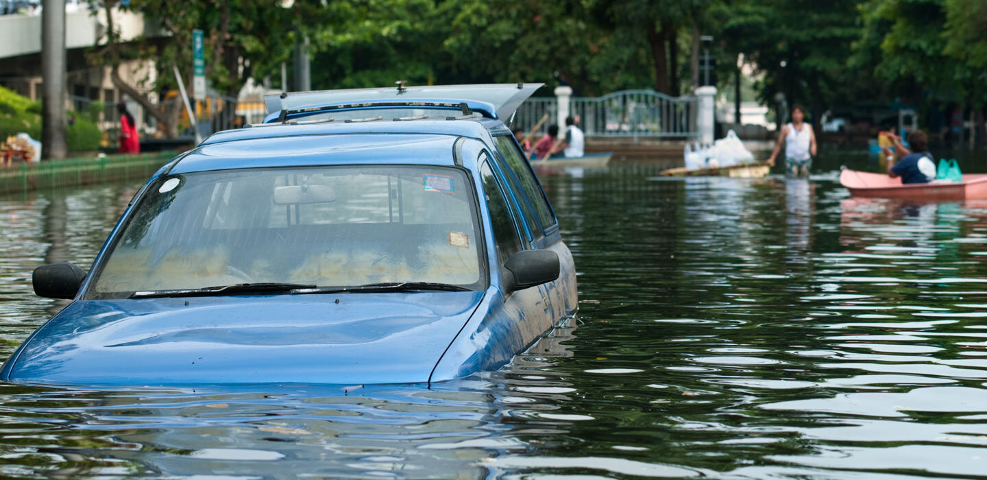 a car is partially submerged in a flooded street while people paddle in boats in the background