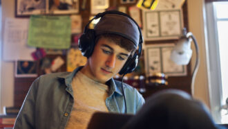 a teen boy wears headphones while working on a laptop