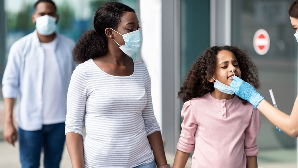 a mom holds her daughters hand during a test swab for COVID