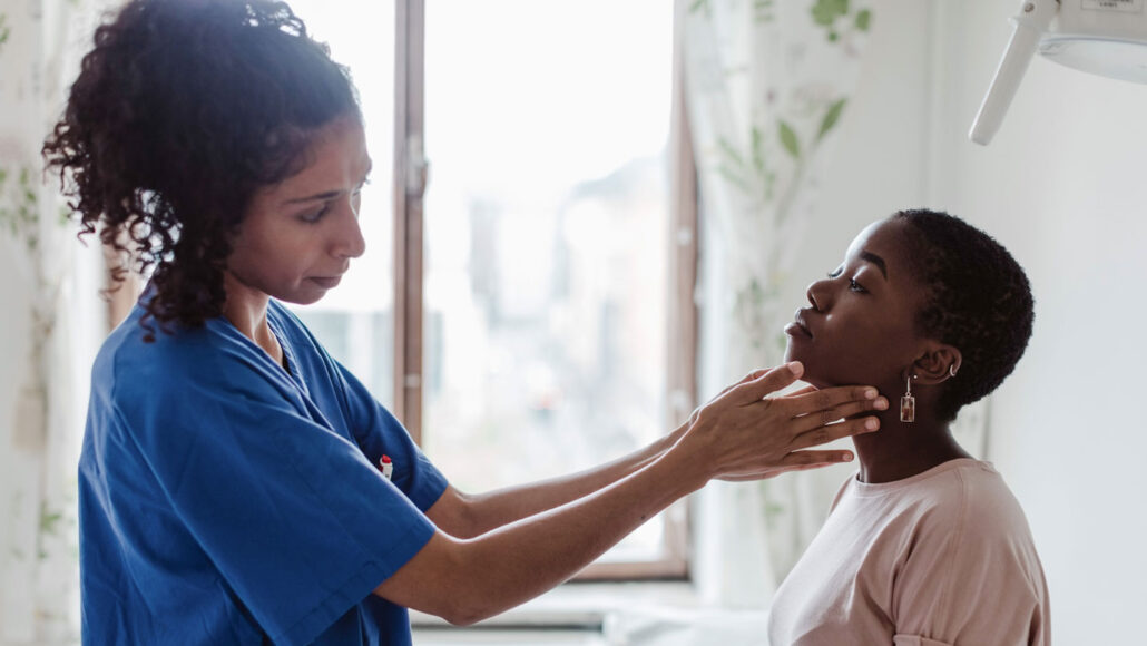 a doctor presses her fingertips against the sides of her patient's throat as part of a checkup