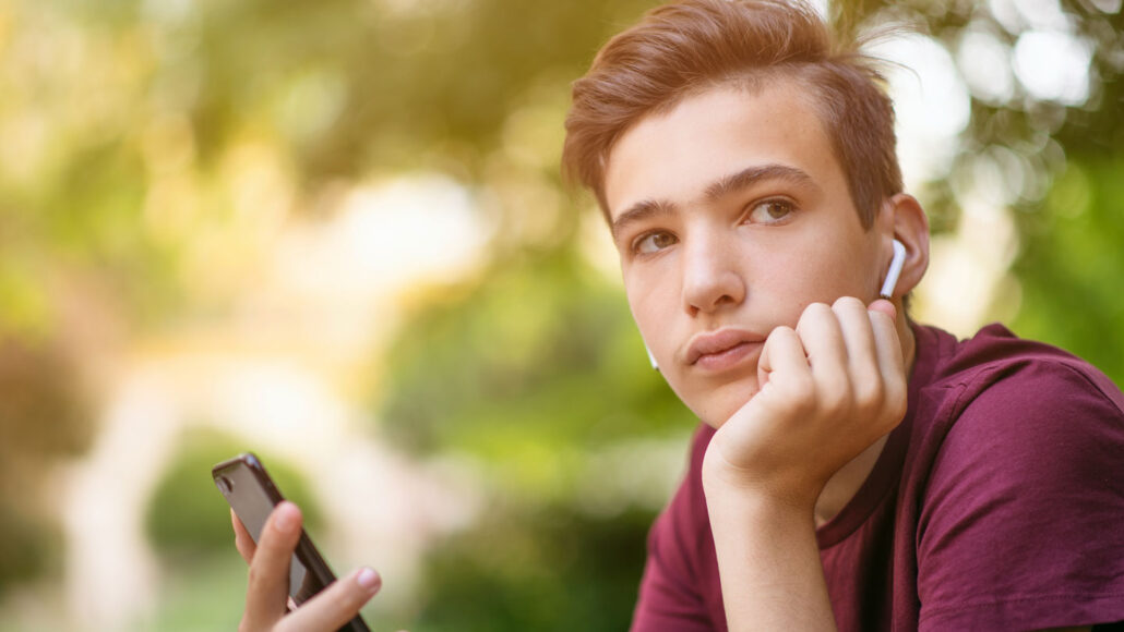 teen boy wearing headphones and holding an iPhone stares into distance