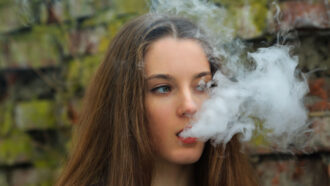 a white teenage girl blows a plume of vape smoke