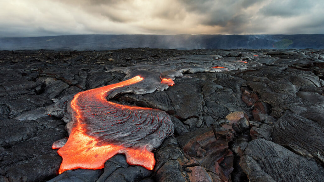 a pool of red-hot lava oozes across a field of hardened, black lava rock