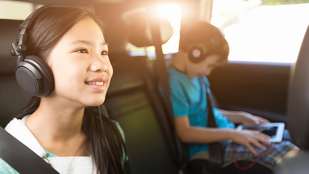 A girl sitting in a car next to her brother listening to headphones