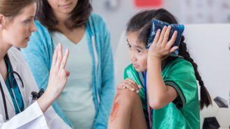 a girl holds an ice pack to her head as a doctor holds up fingers for her to count
