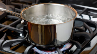 a pot of boiling water is heated by the flames of a gas stovetop