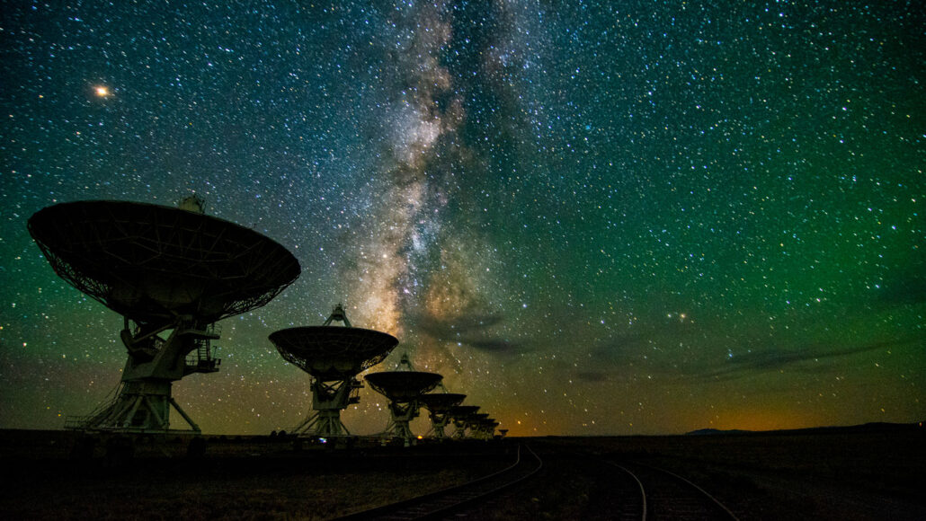 a night time view of the Very Large Array of telescopes with the Milky Way visible in the starry sky overhead
