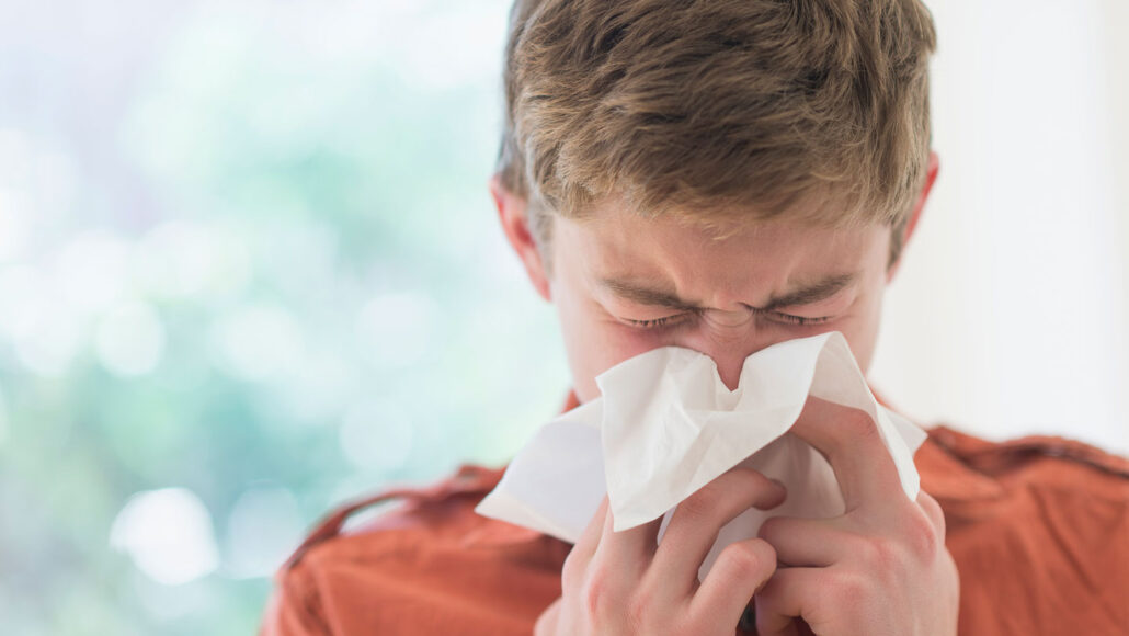 a teenage boy blows his nose into a tissue