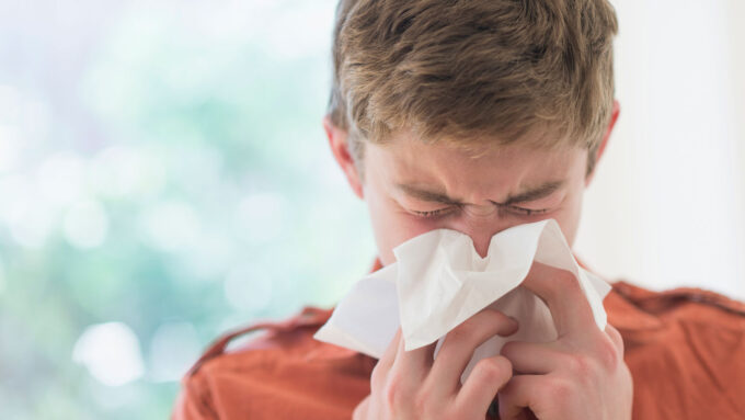 a teenage boy blows his nose into a tissue