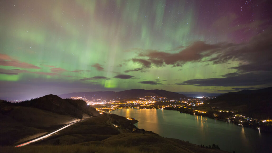 a green aurora shimmers in the sky over a city at night