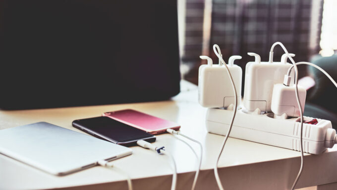 three smartphones on a desk are plugged into a surge protector via charging cables