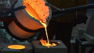 bright orange molten iron being poured from a melting vat into a casting mold